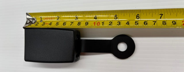 Black rectangular seatbelt buckle with a circular hole on a white background, measured by a yellow tape measure.
