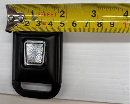 Black seat belt buckle with a measuring tape showing its width on a white background